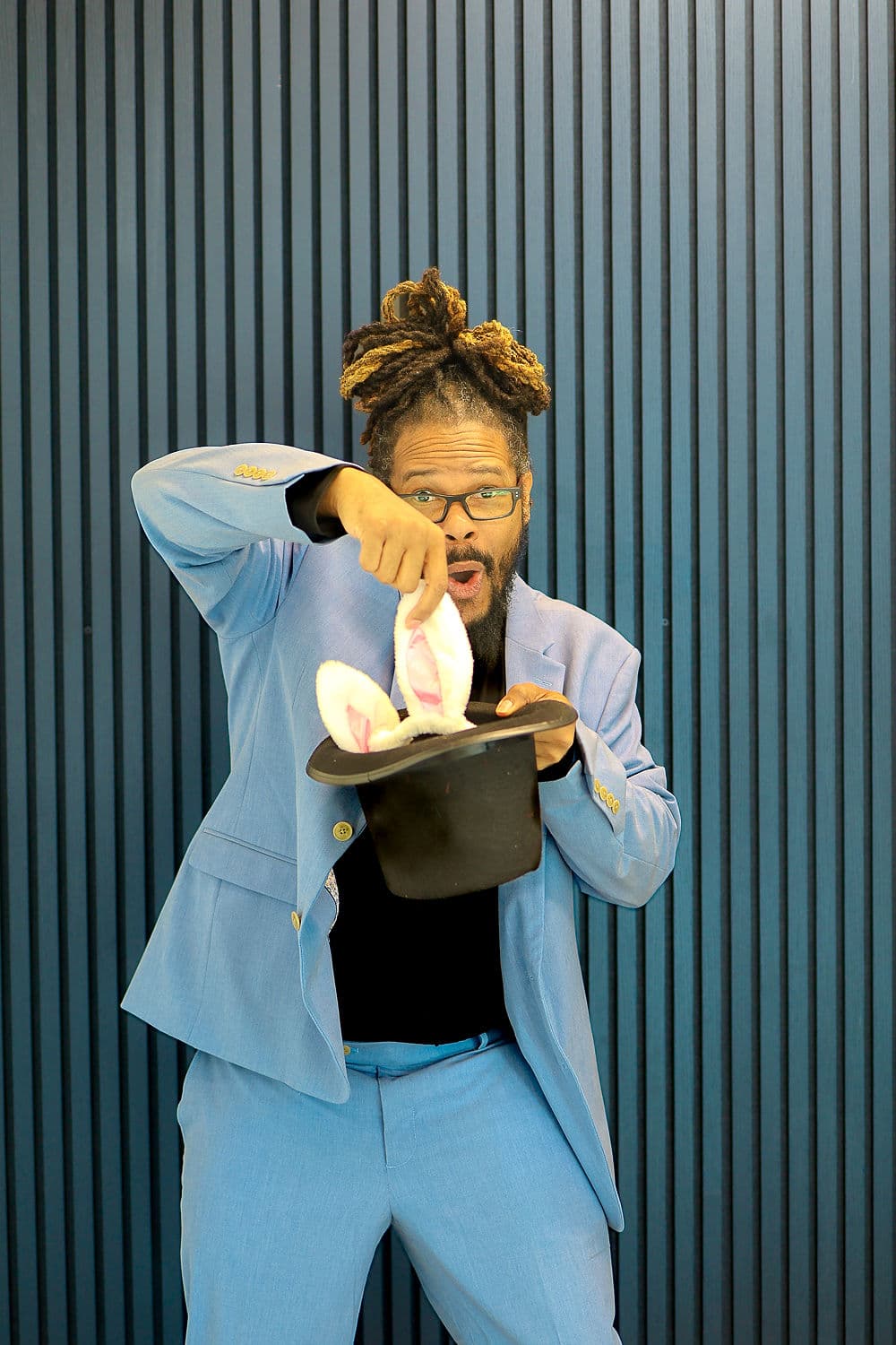 Gregory Rutledge in a blue suit pulling a rabbit out of a top hat